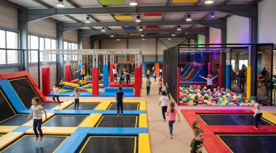 Vue d'ensemble d'un trampoline park moderne montrant plusieurs enfants pratiquant simultanément différentes activités dans diverses zones équipées